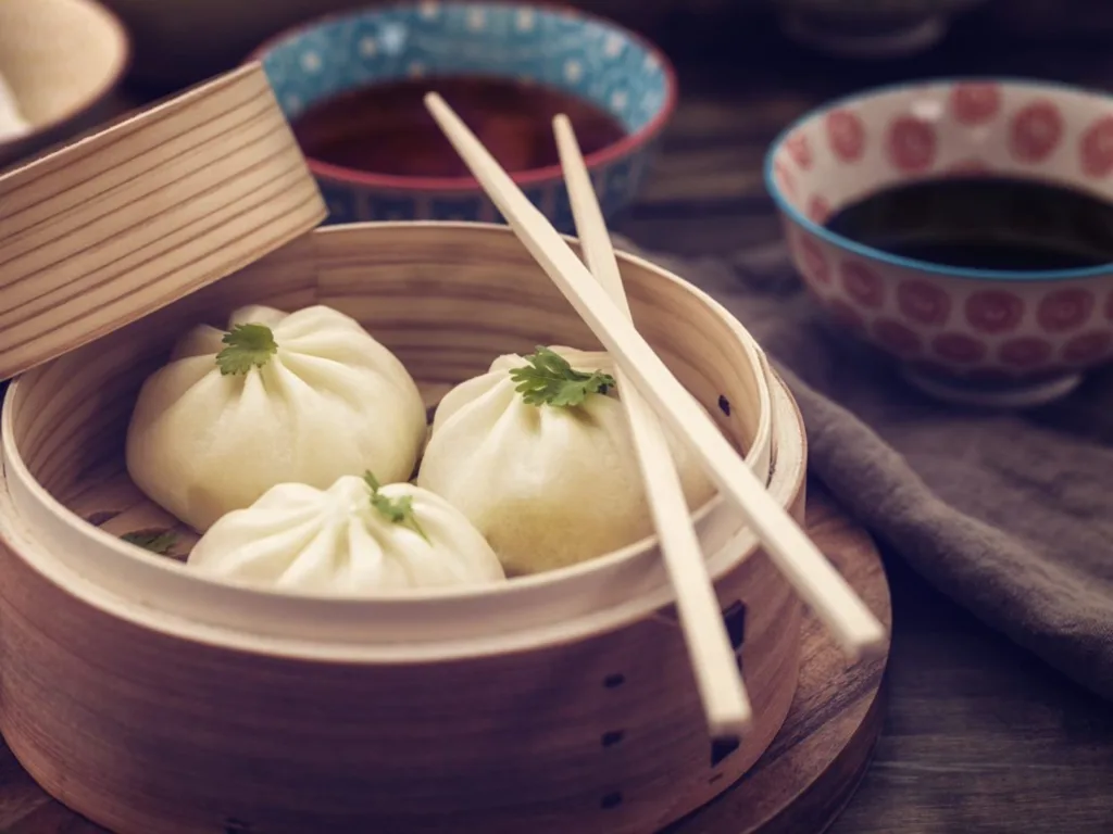 Dim Sum Dumplings Freshly Steamed in a Bamboo Steamer with chopsticks and bowl of sauce