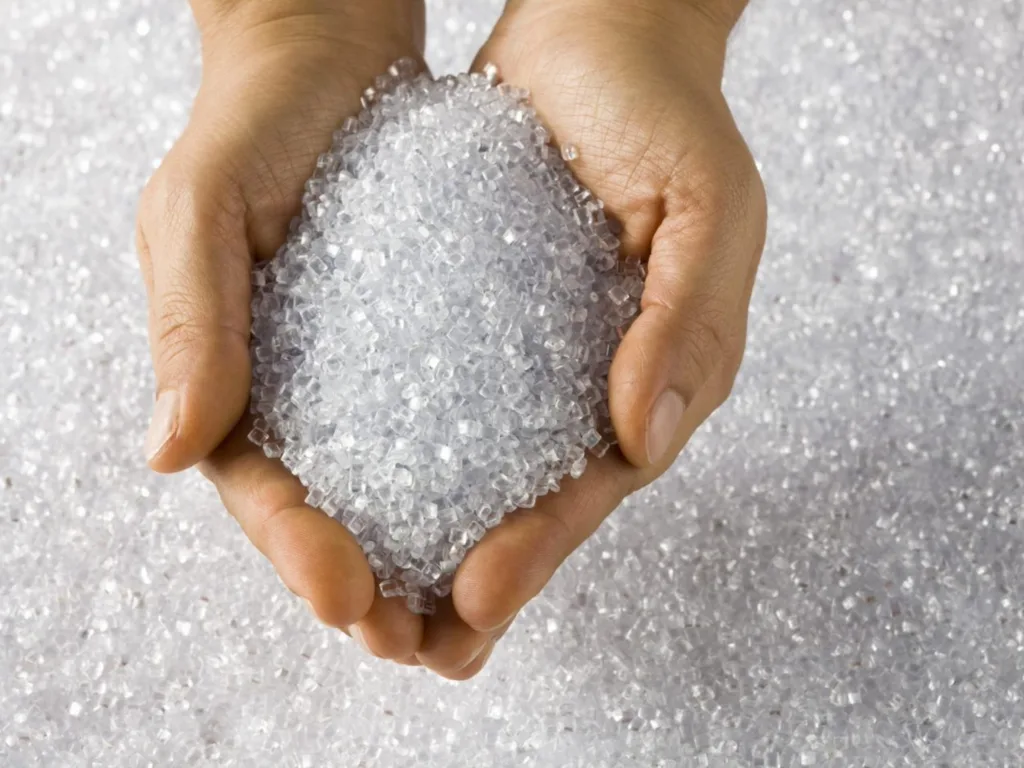 Hands holding granulated sugar above a spread of granulated sugar