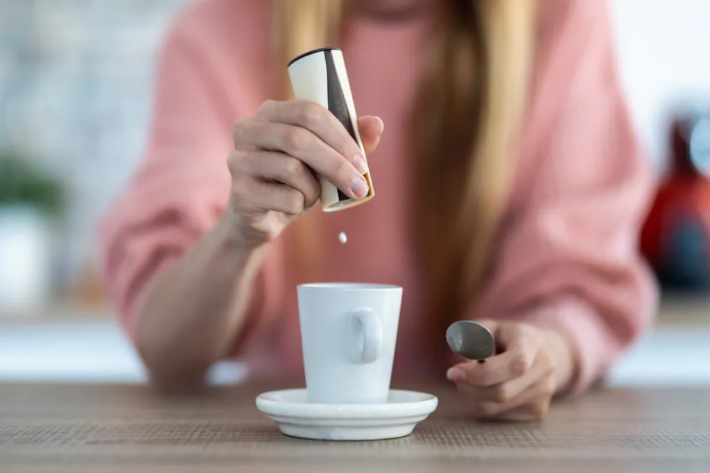 Woman hand throwing saccharin pills on coffee cup in the kitchen at home.